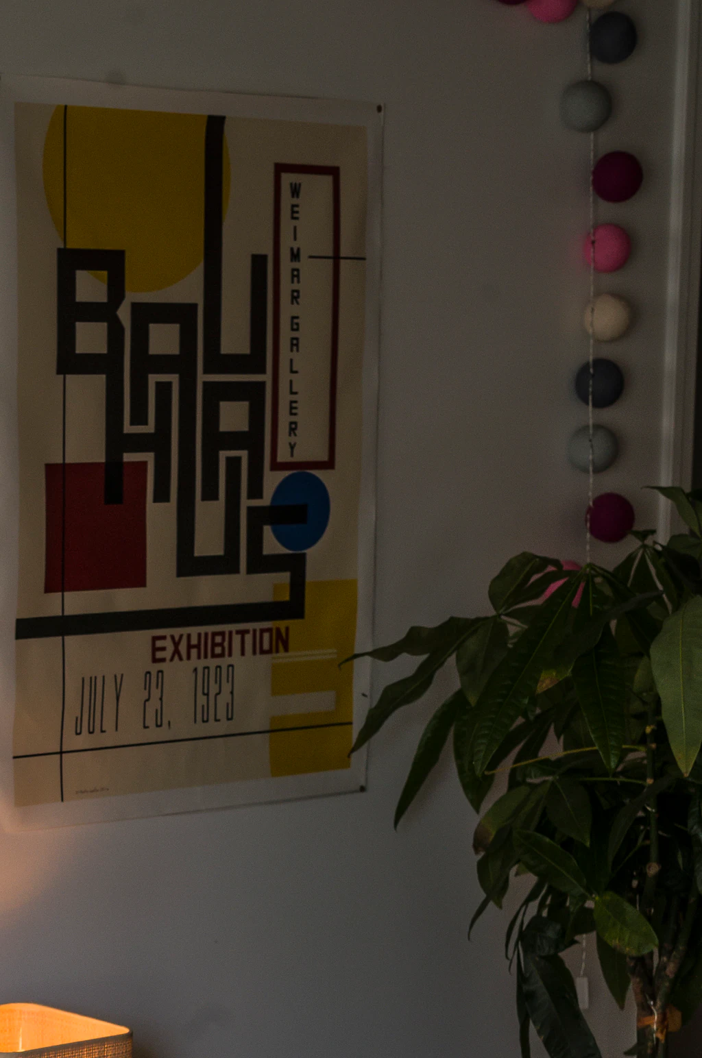 Affiche vintage de l'exposition Bauhaus à la Weimar Gallery, datée du 23 juillet 1923, accrochée près d'une guirlande de pompons colorés et d'une plante verte
